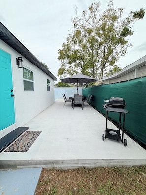 An outdoor patio with a grill, table, chairs, and a covered umbrella. - Spacious Black Luxe Retreat with 2 Kitchens, 2 Master Suites & Luxury Comfort (Tampa)