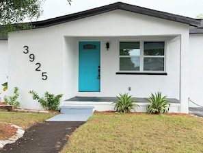 A single-story house with a blue door, numbered 3925, and a small front porch with steps. - Spacious Black Luxe Retreat with 2 Kitchens, 2 Master Suites & Luxury Comfort (Tampa)