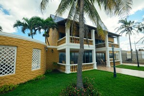 Un bâtiment à deux étages doté d’un balcon, entouré de palmiers et d’une pelouse bien entretenue.