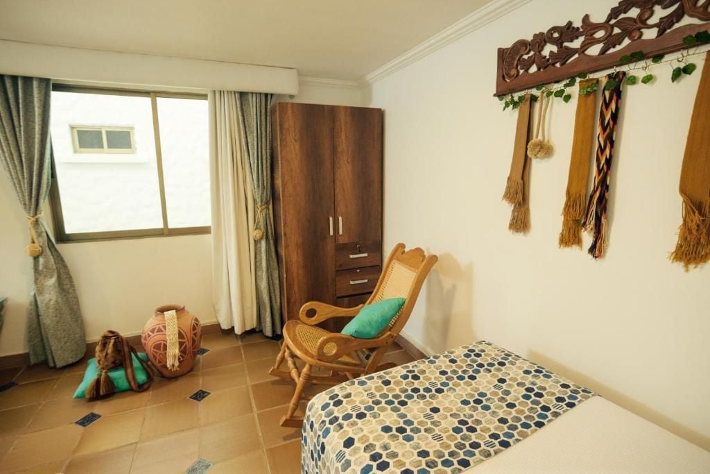 Un dormitorio con cama, armario, silla y ventana con cortinas.