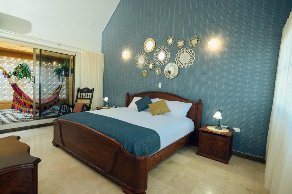 Une chambre avec un grand lit, une table de chevet, une chaise et un hamac visible à travers une porte vitrée.