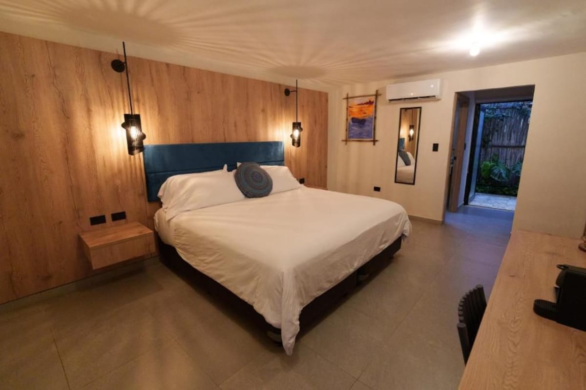 Une chambre à coucher comprenant un lit, des tables de chevet, une tête de lit en bois et un appareil de climatisation.