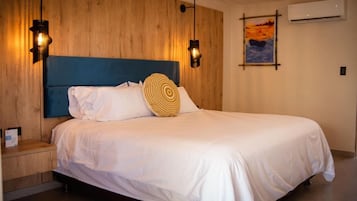 Habitación de hotel con cabecera de madera, cama con ropa blanca, dos lámparas de pared y un cuadro en la pared.