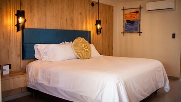 Habitación de hotel con cabecera de madera, cama con ropa blanca, dos lámparas de pared y un cuadro en la pared.