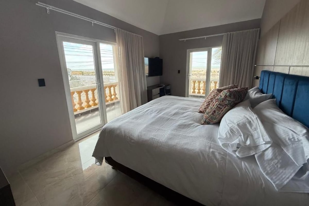 Une chambre avec un grand lit, deux fenêtres avec des rideaux, un téléviseur à écran plat et une vue sur le balcon.