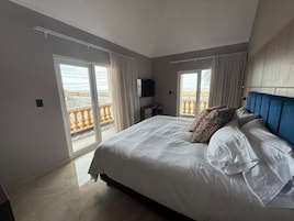 Un dormitorio con una cama grande, dos ventanas con cortinas, un televisor de pantalla plana y vistas al balcón.
