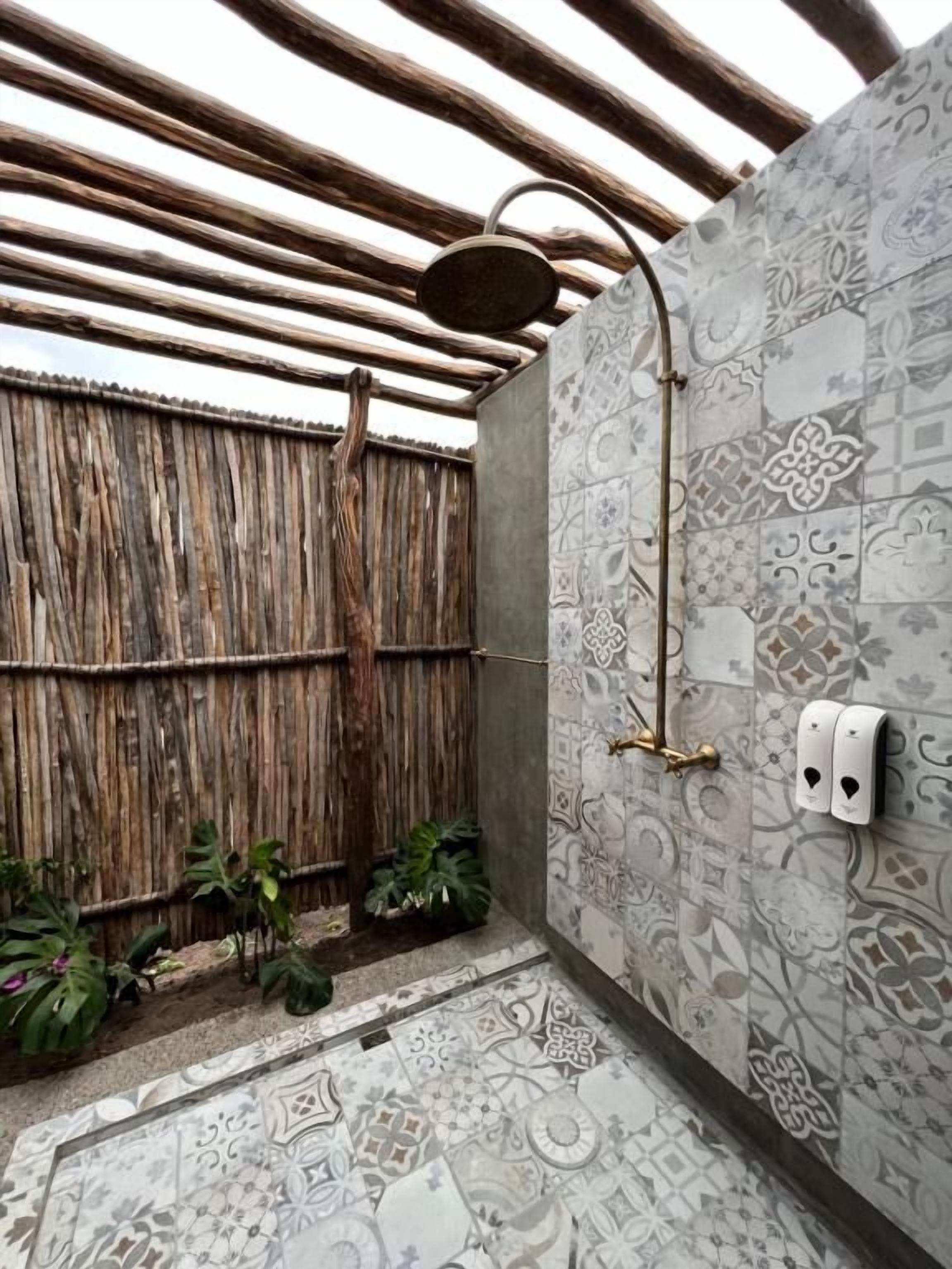 A shower area with a patterned tile wall, a wooden ceiling, and a bamboo fence.
