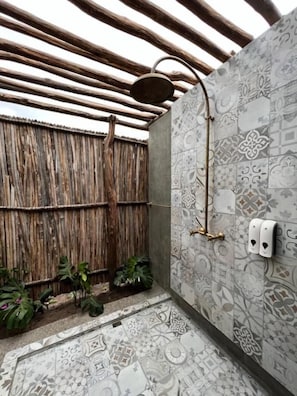 Un espace douche avec un mur recouvert de carreaux à motifs, un plafond en bois et une clôture en bambou.