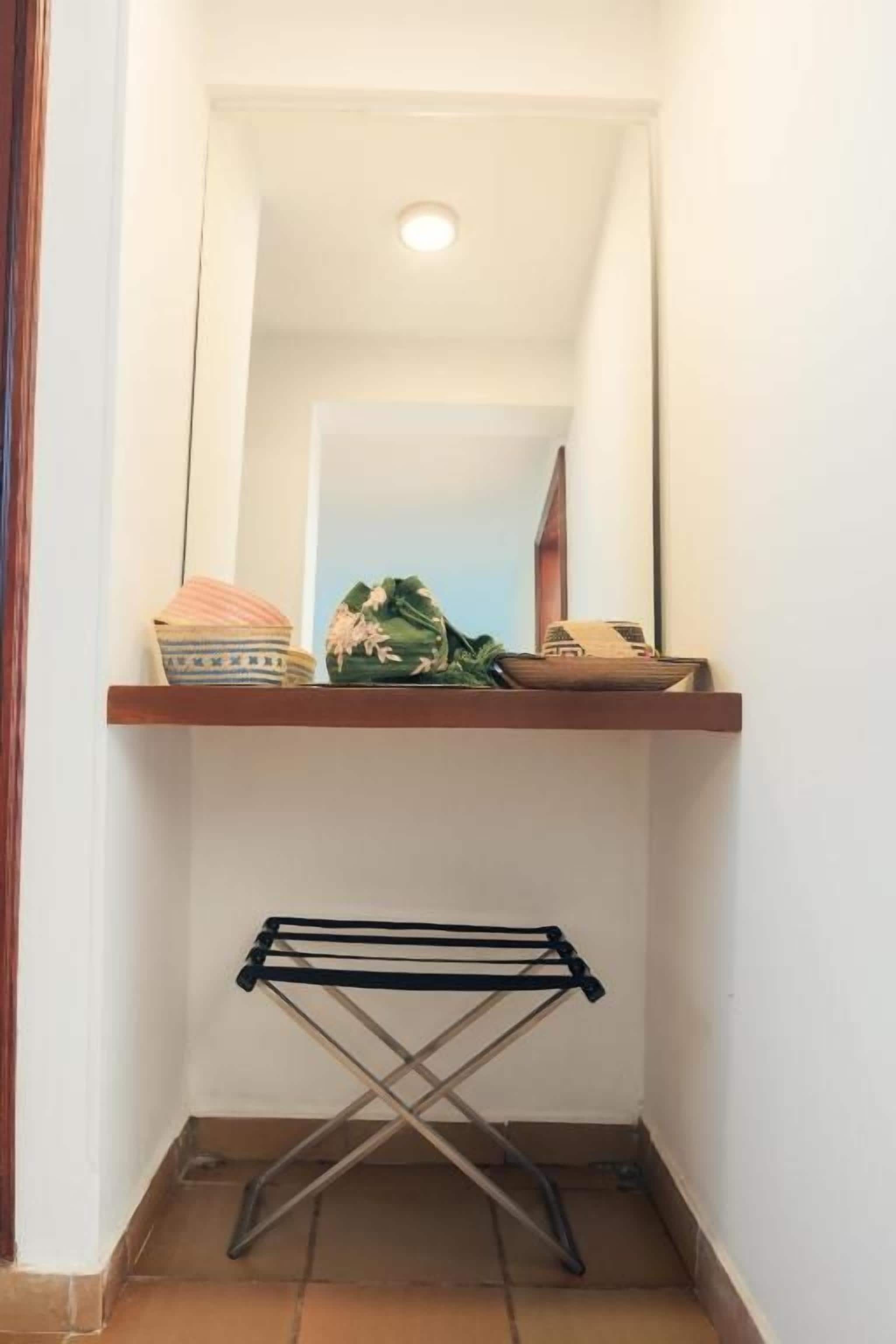A narrow hallway with a mirror, a shelf with a decorative item, and a drying rack.