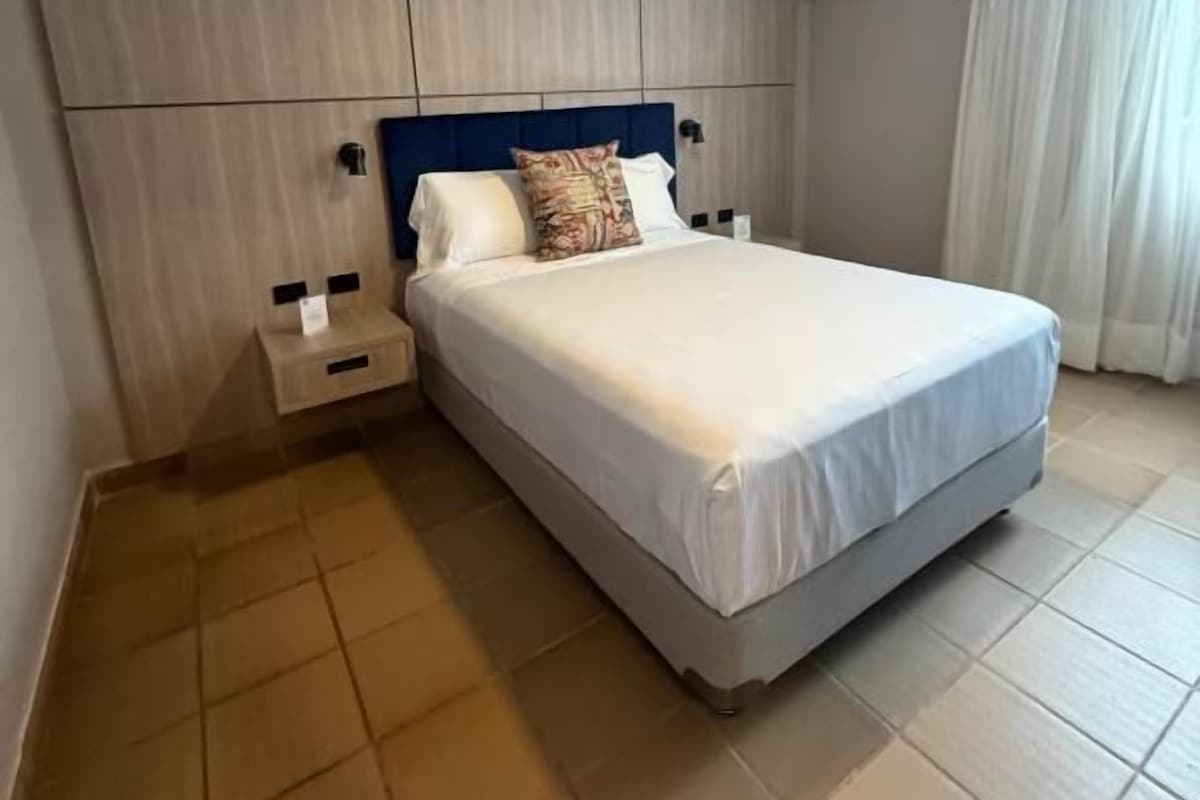 Une chambre d’hôtel avec un grand lit, une table de chevet, un climatiseur fixé au mur et une fenêtre avec des rideaux.