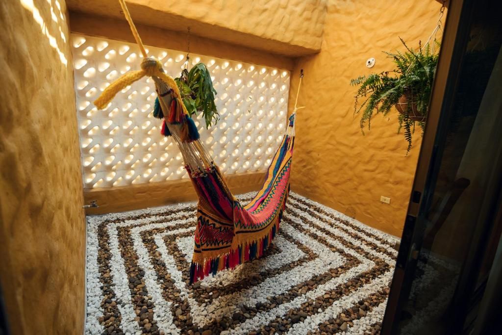 A hammock suspended from a wooden ceiling, a patterned rug on the floor, and a wall with a perforated design.