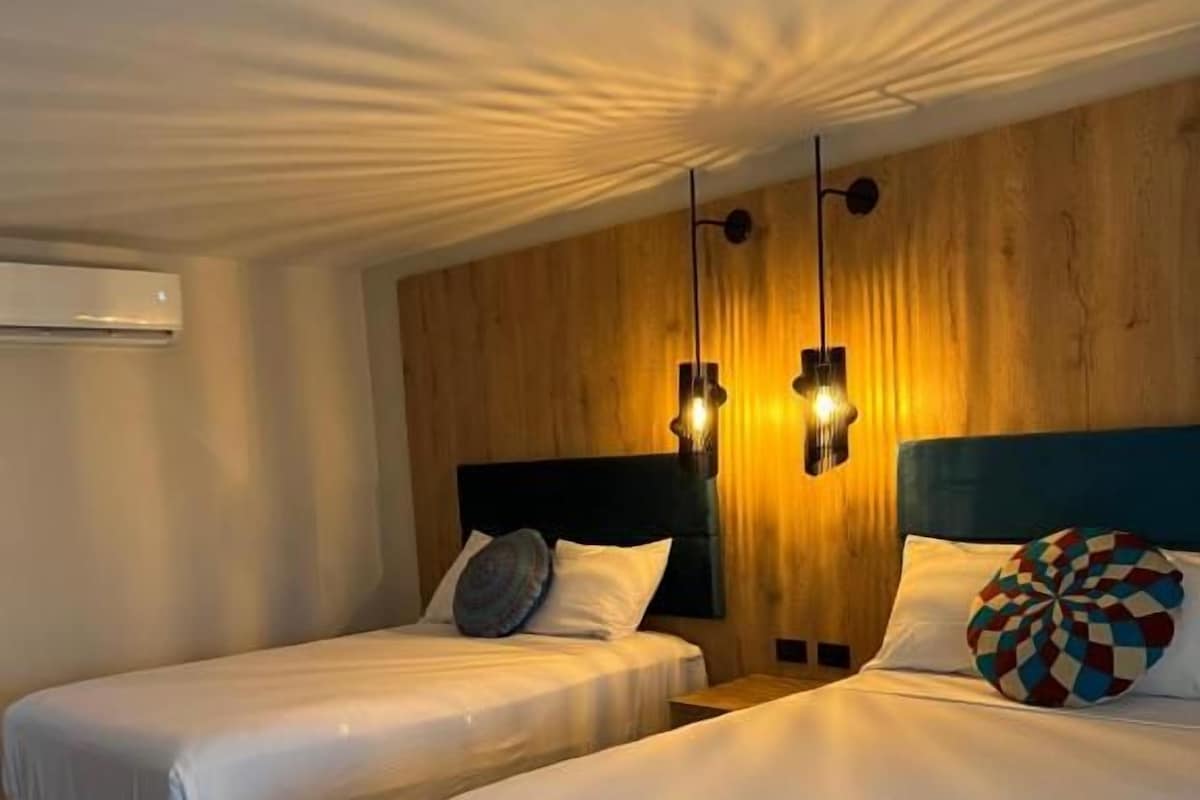 Une chambre d’hôtel avec deux lits, un lambris en bois sur le mur et des luminaires suspendus.