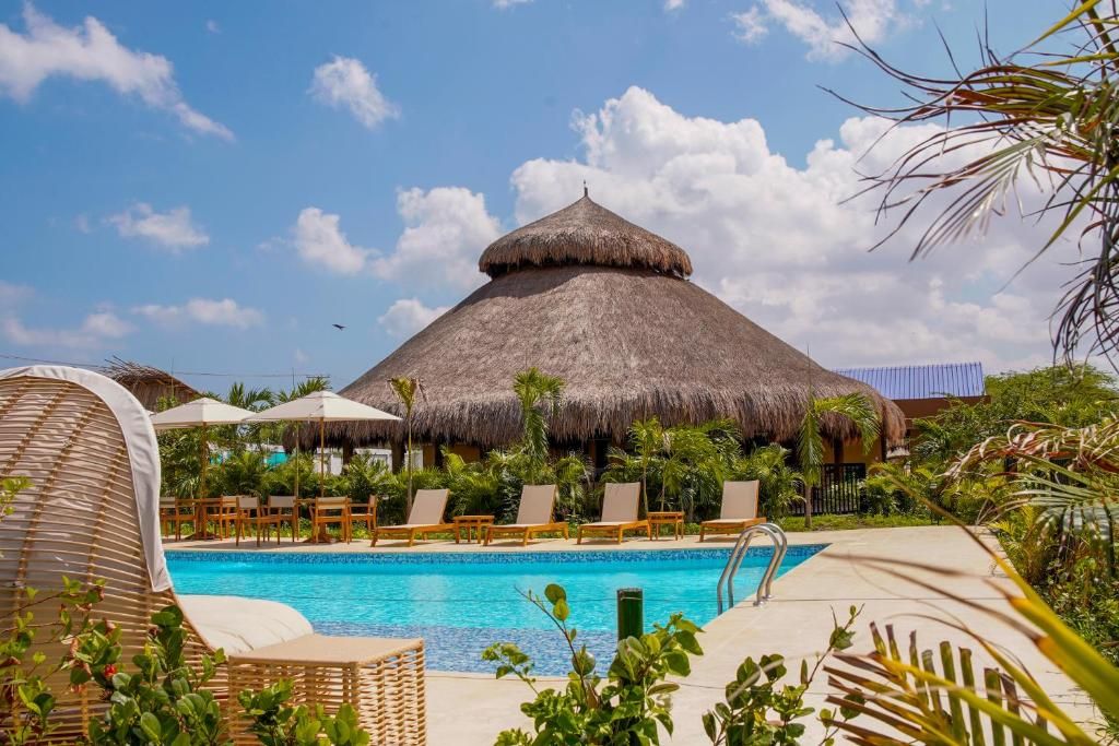 A pool area with lounge chairs, a thatched-roof structure, and tropical vegetation.