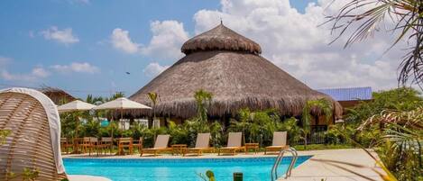 A pool area with lounge chairs, a thatched-roof structure, and tropical vegetation.