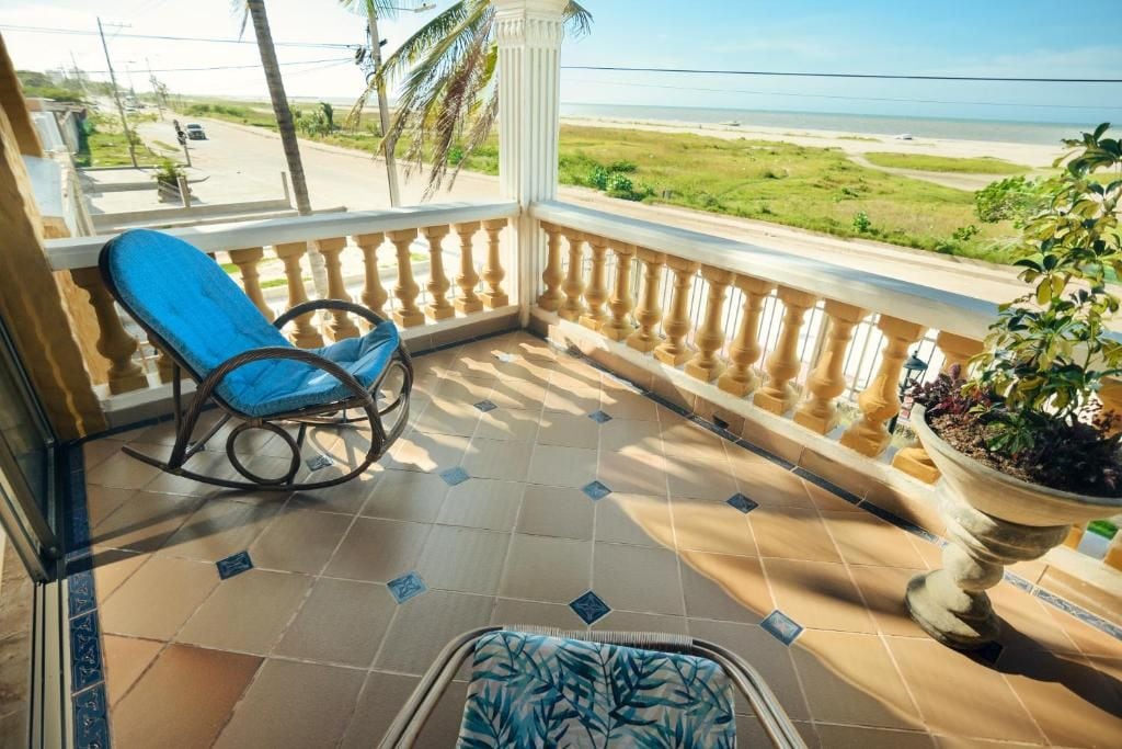 Ein Balkon mit einem Schaukelstuhl, einer Topfpflanze und Blick auf den Strand.
