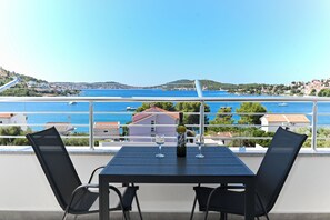 Ein Tisch mit zwei Stühlen und einer Weinflasche auf einem Balkon mit Blick auf die Küste, wo Boote und Gebäude zu sehen sind.