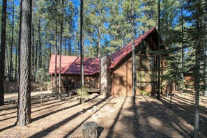 A cabin with a red roof, surrounded by tall pine trees in a forest setting.