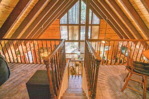 A wooden staircase leading to a loft bedroom with a large window overlooking a forest.