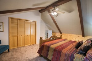 A bedroom with a sloped ceiling, a wooden bed with a colorful striped bedspread, a wooden wardrobe, and a ceiling fan.