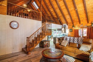 A spacious loft with a wooden staircase, a cozy seating area, and a kitchen in the background.