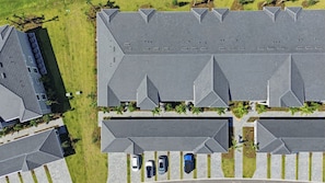 An aerial view of a residential area with multiple houses, a parking lot, and a small green space with palm trees. - Course side Condo - 2BR + Den - Golf Membership Included; Calusa Country Club (Bradenton)