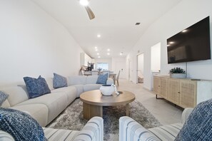 A modern living room with a sectional sofa, a round coffee table, and a flat-screen TV mounted on the wall. - Course side Condo - 2BR + Den - Golf Membership Included; Calusa Country Club (Bradenton)