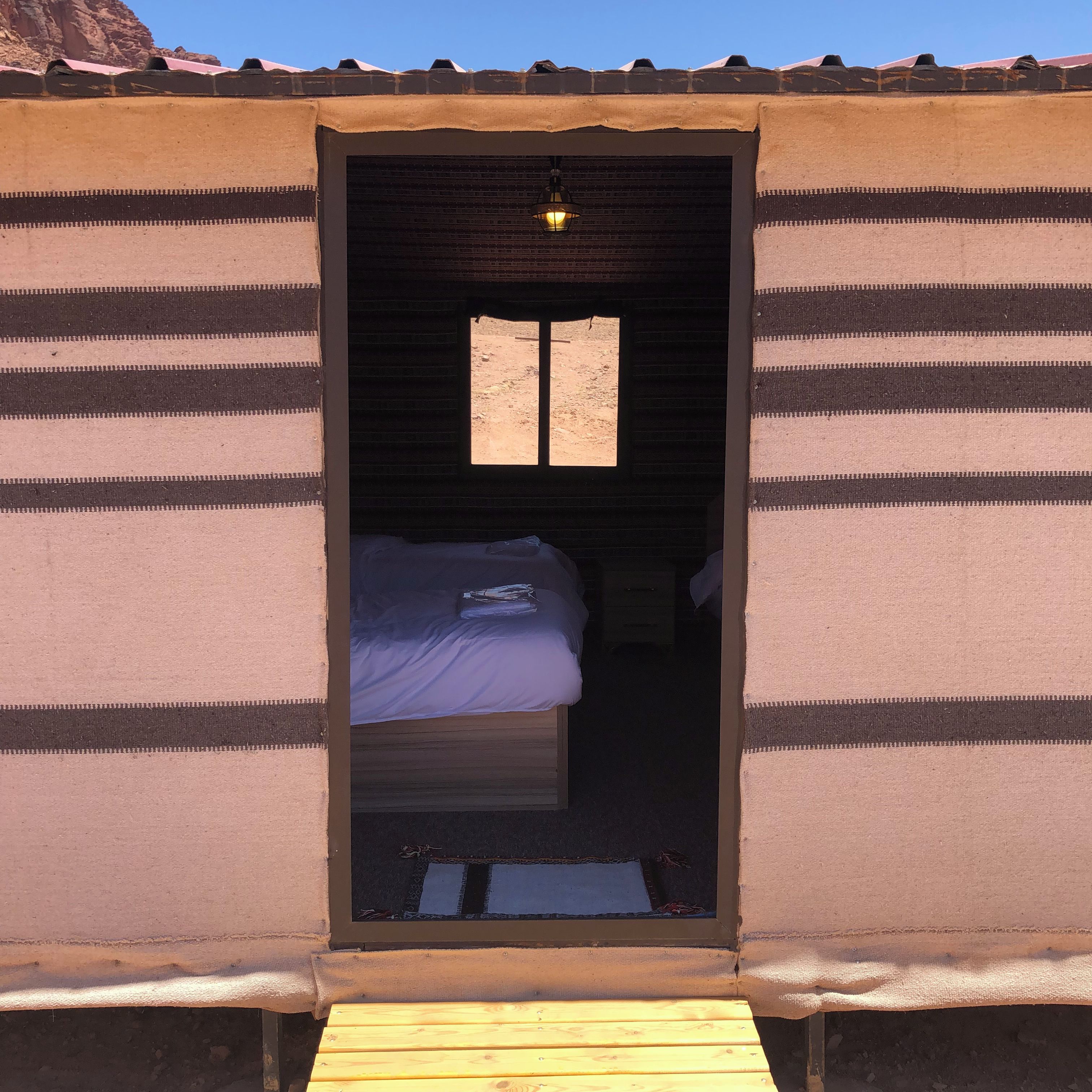 Un umbral conduce a una habitación con cama, ventana y una mesita.