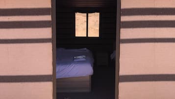 Un umbral conduce a una habitación con cama, ventana y una mesita.