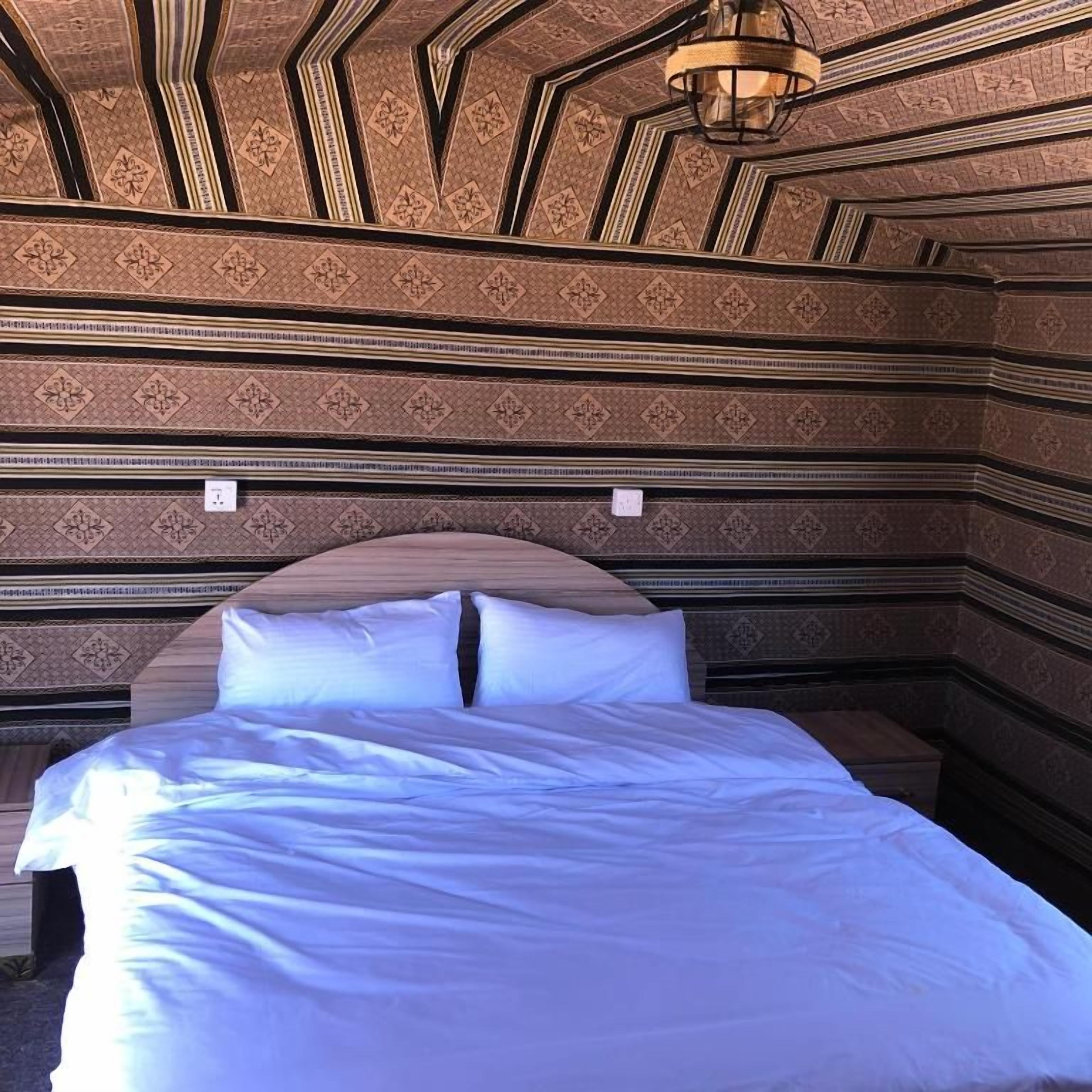 Una habitación con techo estampado, una cama con ropa de cama blanca y una lámpara colgante.