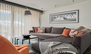 A modern living room with a grey sofa, orange armchair, and a black coffee table. A large window with sheer curtains allows natural light. - STYLISH ALPINE PENTHOUSE NEAR RESTAURANTS & MOUNTAIN RAILWAYS (Zermatt)