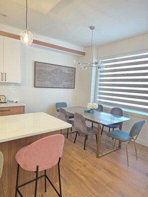A modern kitchen with a dining area, wooden flooring, and a large window with blinds. - Fort Casamingo 3 bedroom, 3 full bath beautiful home/ Free Wifi (Fort Saskatchewan)