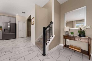 A modern kitchen with a stainless steel refrigerator, a marble-tiled floor, and a staircase with a black railing. - Family Paradise | 6BR | Near Disney (Davenport)