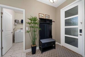 Un couloir avec une porte donnant sur une buanderie, une plante en pot, un meuble en bois foncé et une porte en verre à motifs dépolis.