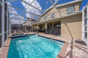 A swimming pool with a covered patio area, a building with a beige exterior, and a clear sky. - Family Paradise | 6BR | Near Disney (Davenport)