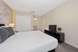 Une chambre d’hôtel avec un grand lit, un téléviseur posé sur un meuble, une armoire et une salle de bain visible à travers une porte ouverte.