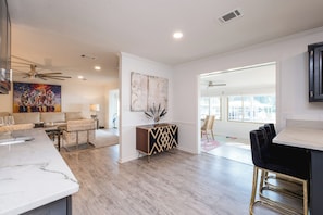 A modern kitchen with a marble countertop, a dining area with a bar, and a living room with a sofa and a painting. - Charming 3-bedroom 2 bath house on Lake Hamilton in Hot Springs (Hot Springs)