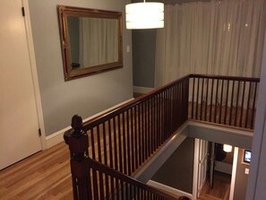Una escalera con barandilla de madera, un espejo en la pared y una lámpara colgante.