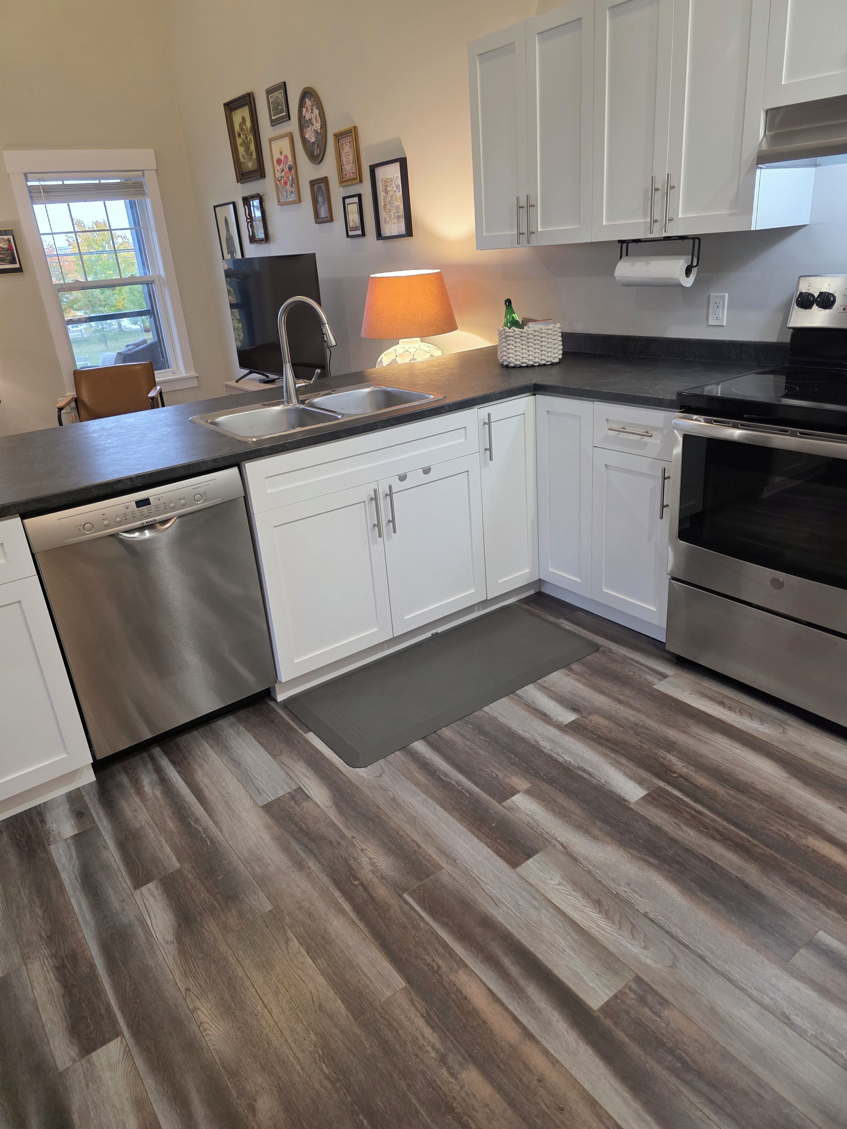 Cocina moderna con armarios blancos, electrodomésticos de acero inoxidable y piso de madera.