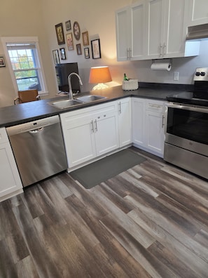 Cocina moderna con armarios blancos, electrodomésticos de acero inoxidable y piso de madera.