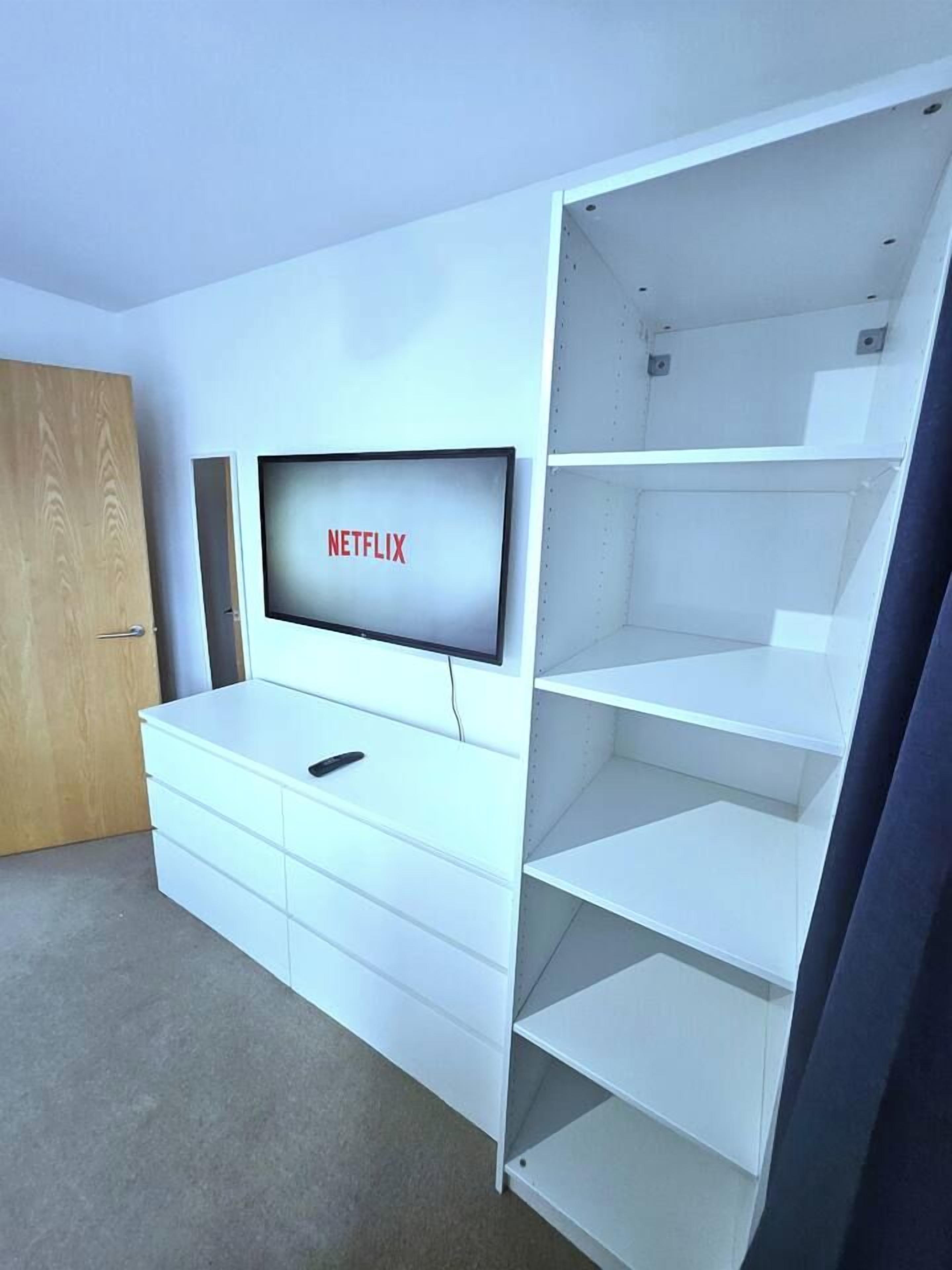 Ett rum med en vit möbel för underhållningssystemet, en tv-skärm som visar ”NETFLIX”, och en dörr.