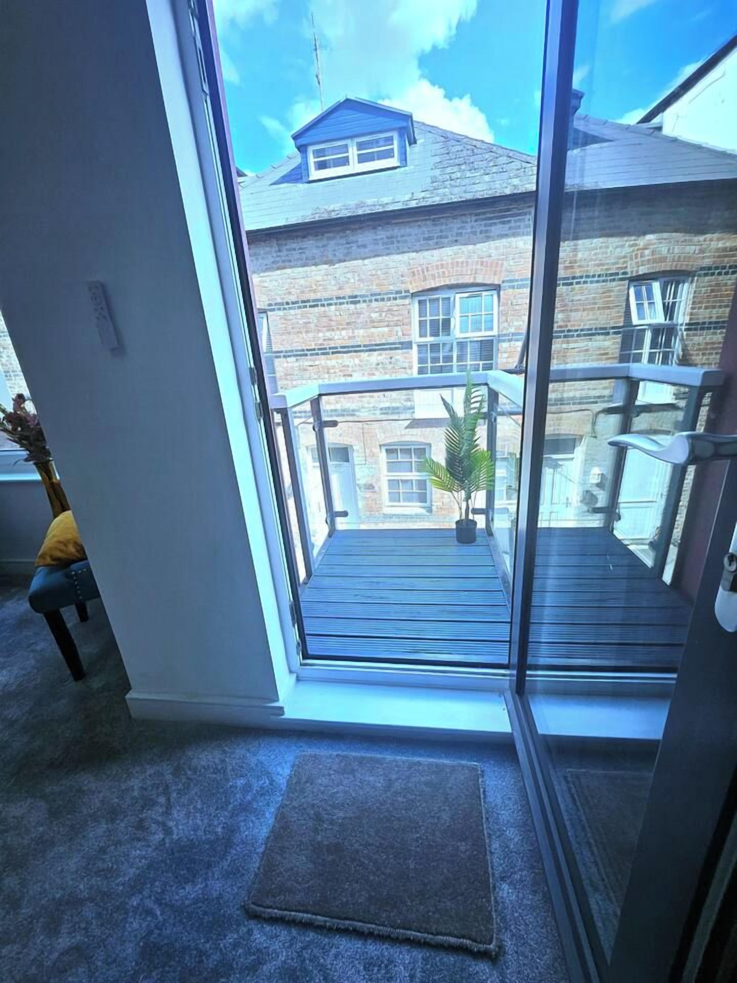 Une pièce dotée d’une grande porte-fenêtre coulissante donnant sur un balcon avec vue sur un immeuble en briques.