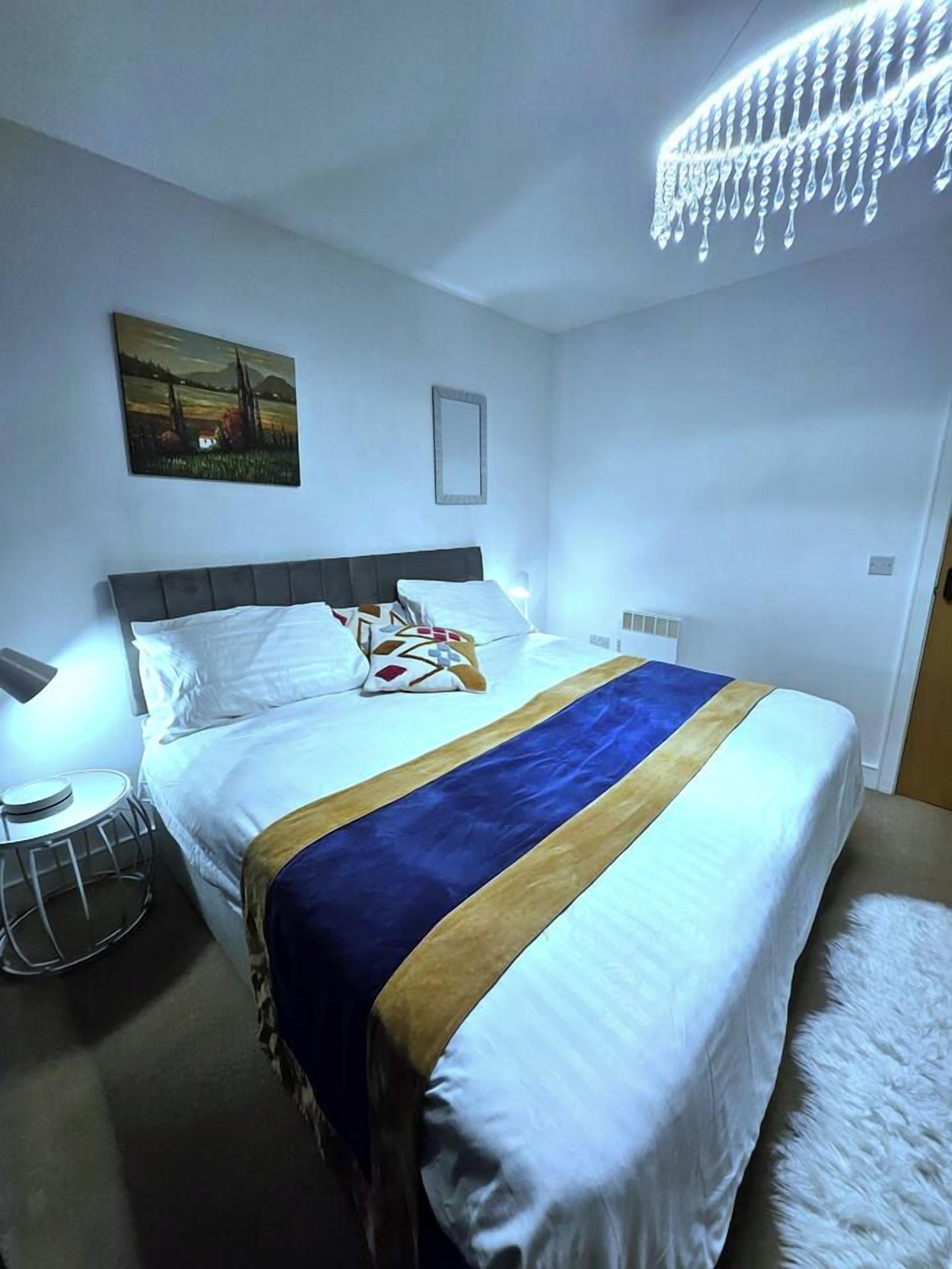 A hotel room with a bed, a bedside table, a lamp, and a painting on the wall.