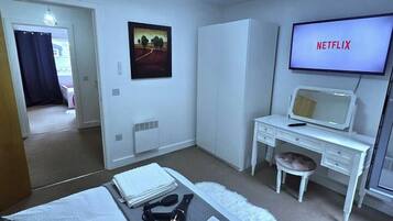 A hotel room with a bed, a desk, a chair, a television displaying 'NETFLIX,' and a wall-mounted mirror.