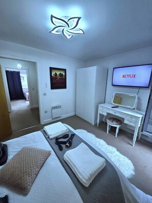 Ett hotellrum med en säng, ett skrivbord, en stol, en tv som visar ”NETFLIX” och en spegel som är monterad på väggen.