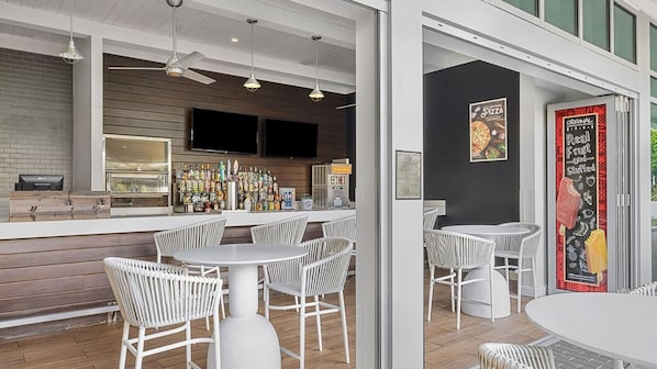 Ein moderner Barbereich mit weißen Korbstühlen, einer Bar und einer Tafel mit der Speisekarte.