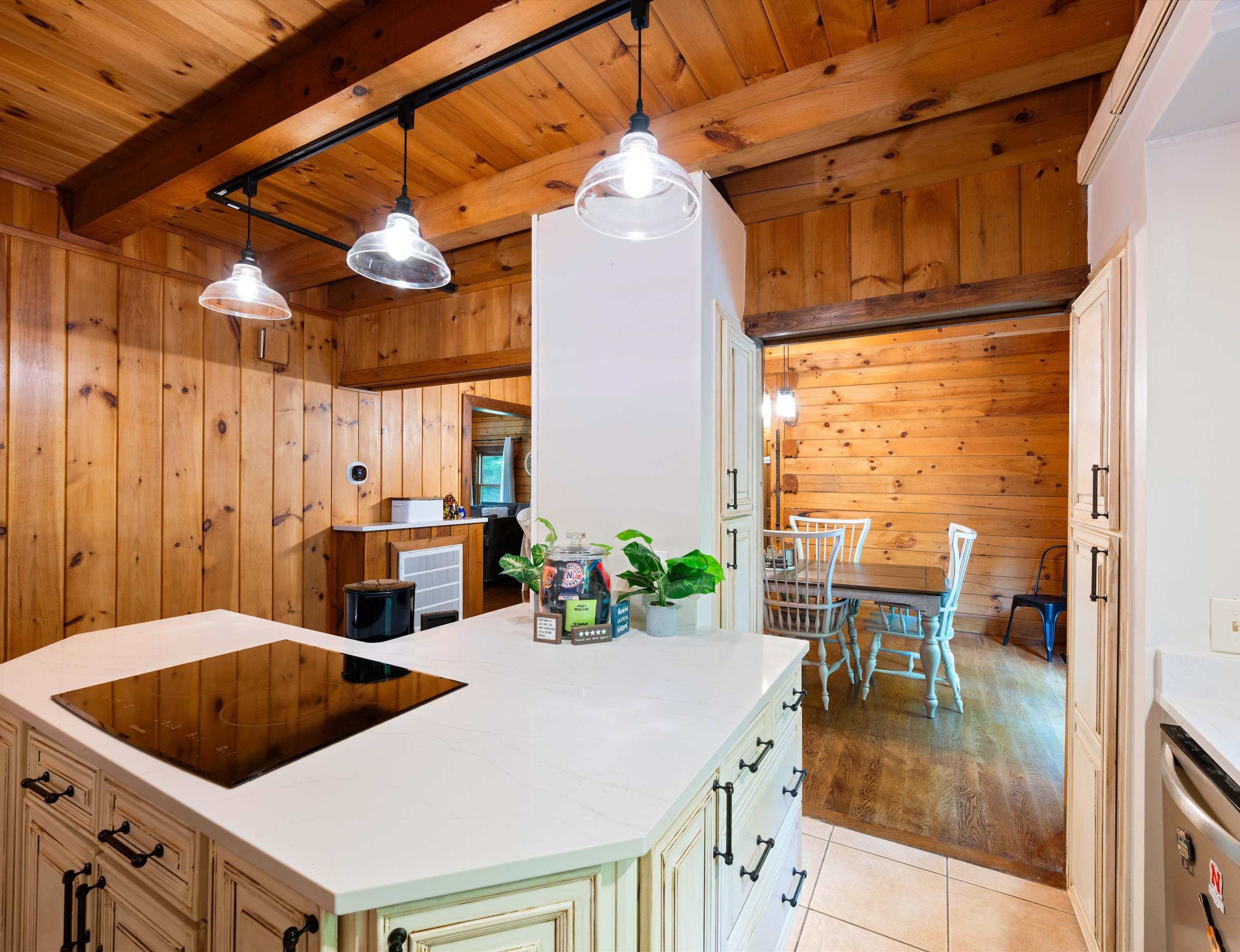 A kitchen with wooden paneling, a central island, pendant lighting, and a view into the dining area.