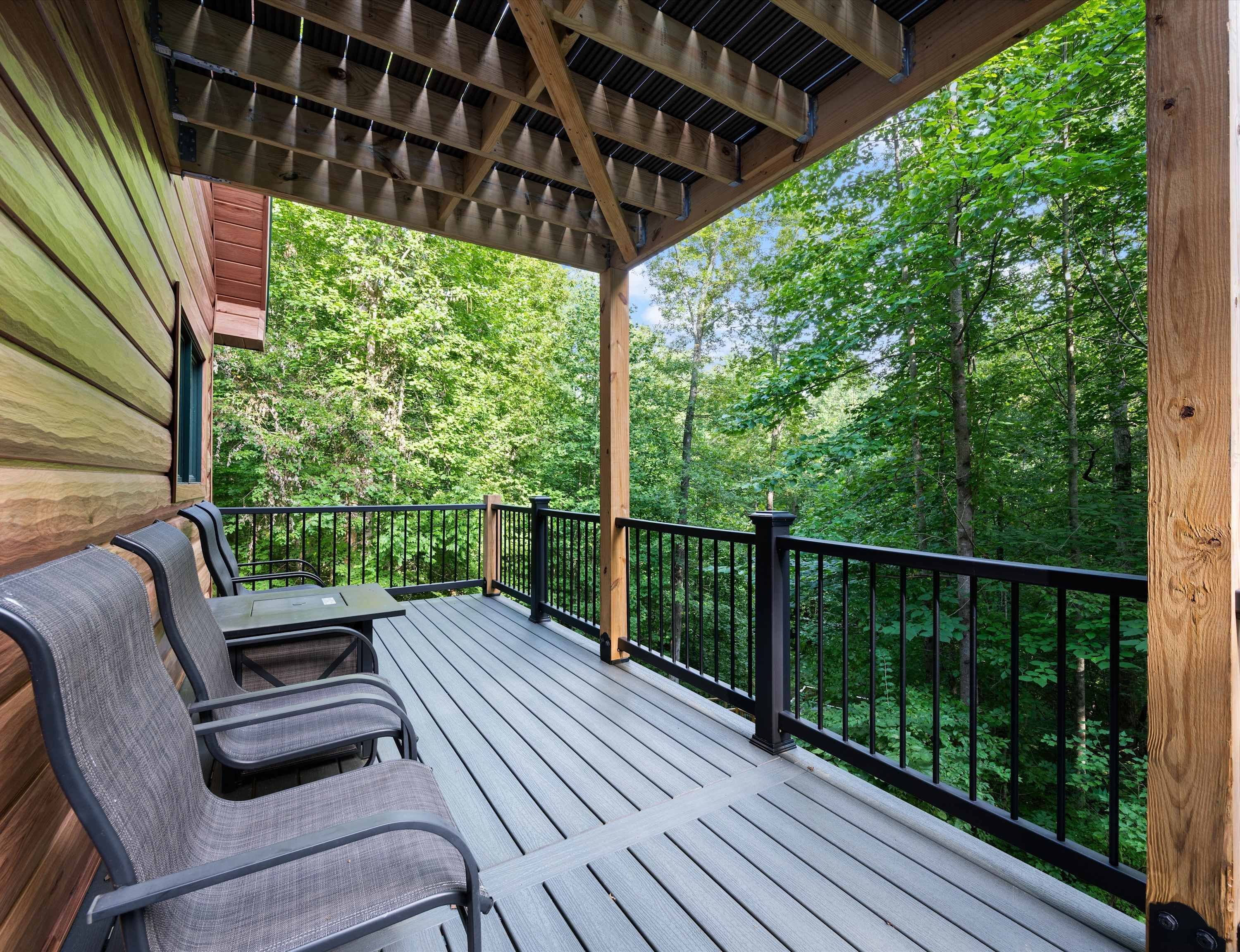A covered deck with seating and a view of a forest.