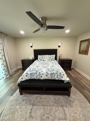Ein Schlafzimmer mit einem Bett, einem Deckenventilator, Nachttischen, einem Teppich und einem Bild an der Wand.