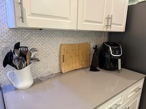 Eine Küche mit weißen Schränken, einem Holzschneidebrett, einer Kaffeemaschine und einem Besteckhalter.