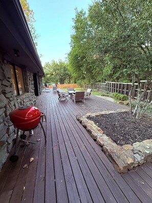 Una terraza de madera con una parrilla, mobiliario exterior y un muro de piedra.